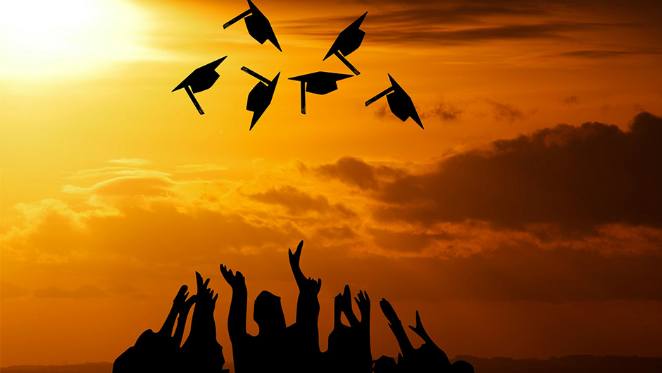 Graduation caps thrown in air with sun and outstretched hands