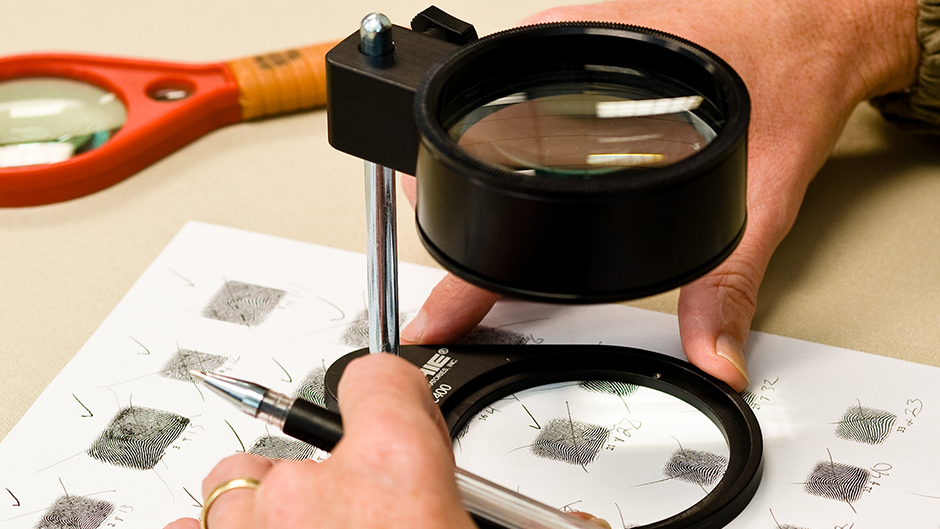 A person examining fingerprints through a microscope