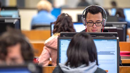 Student looking at computer in library with headphones on